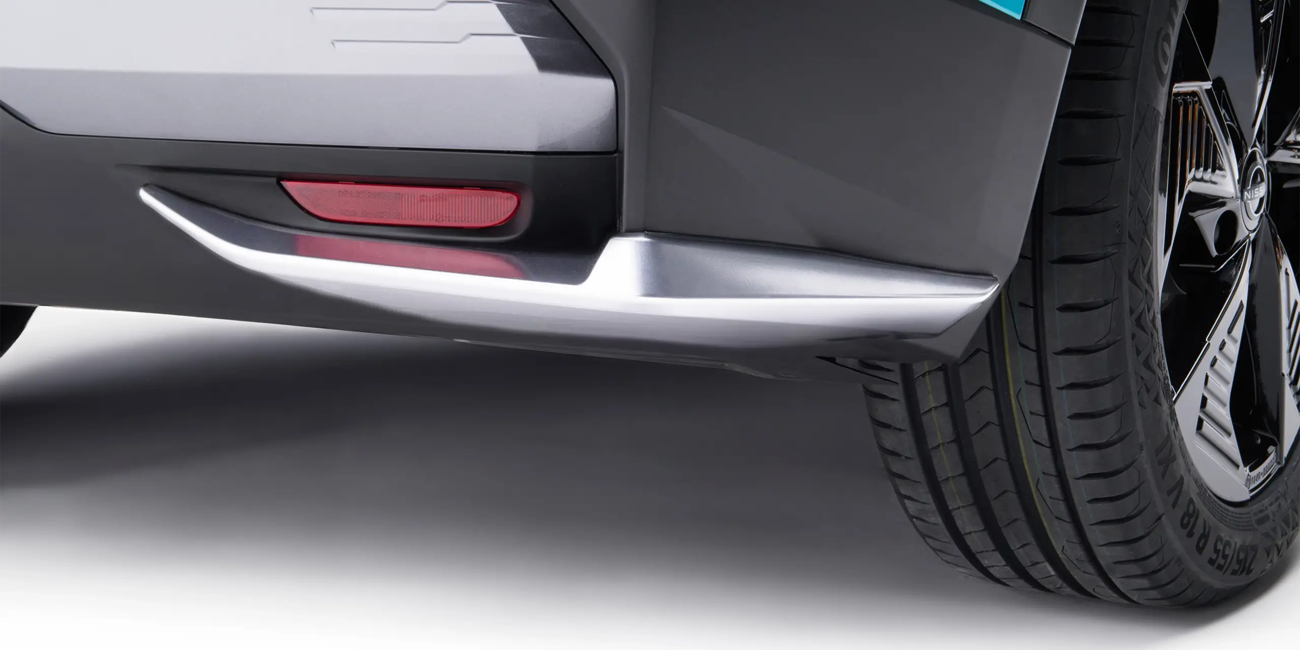 Close-up of a car's rear bumper with a red reflector and a rear tire, showcasing the vehicle's lower body design.