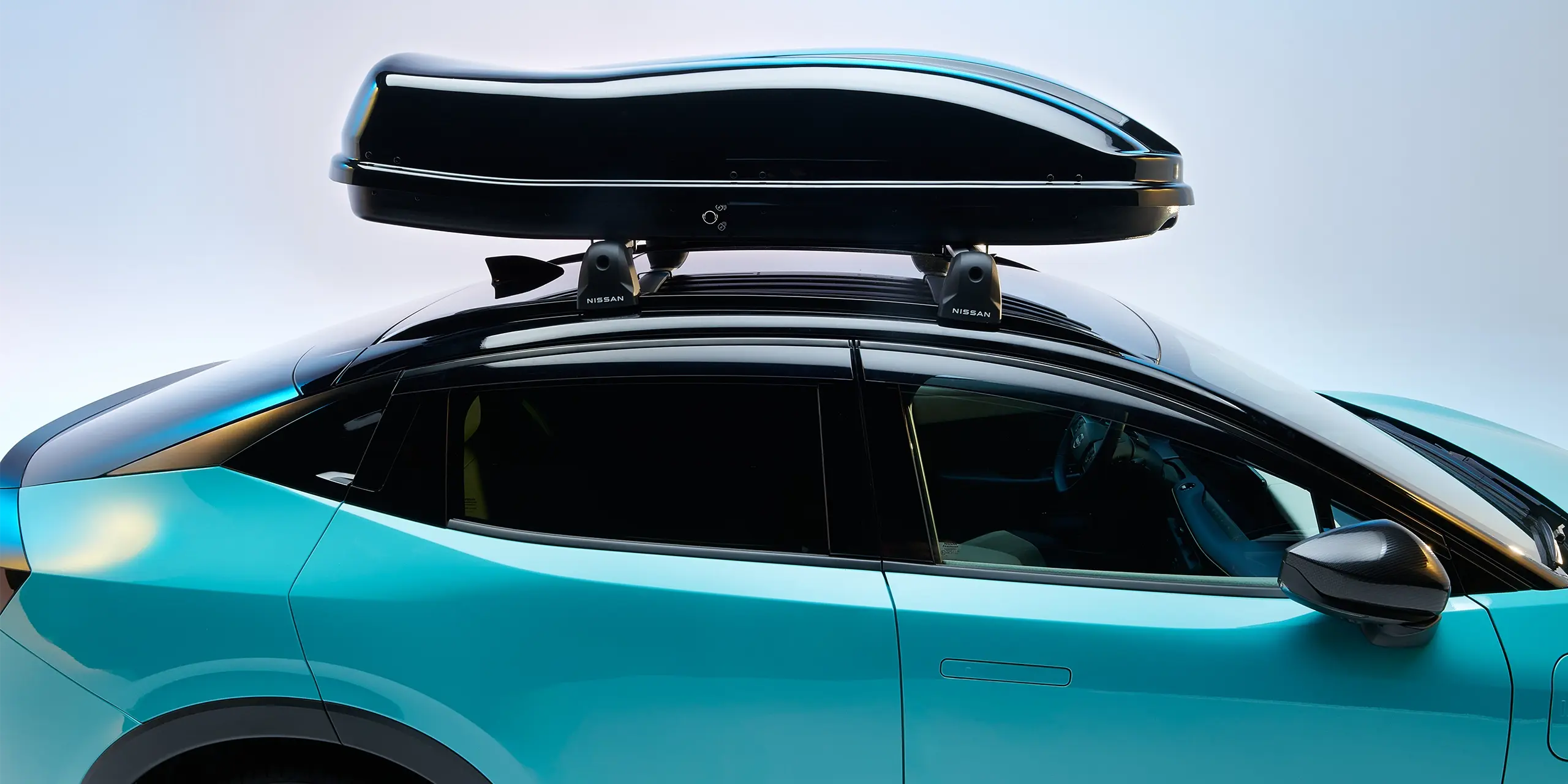 A turquoise car with a black roof box attached to its roof racks.