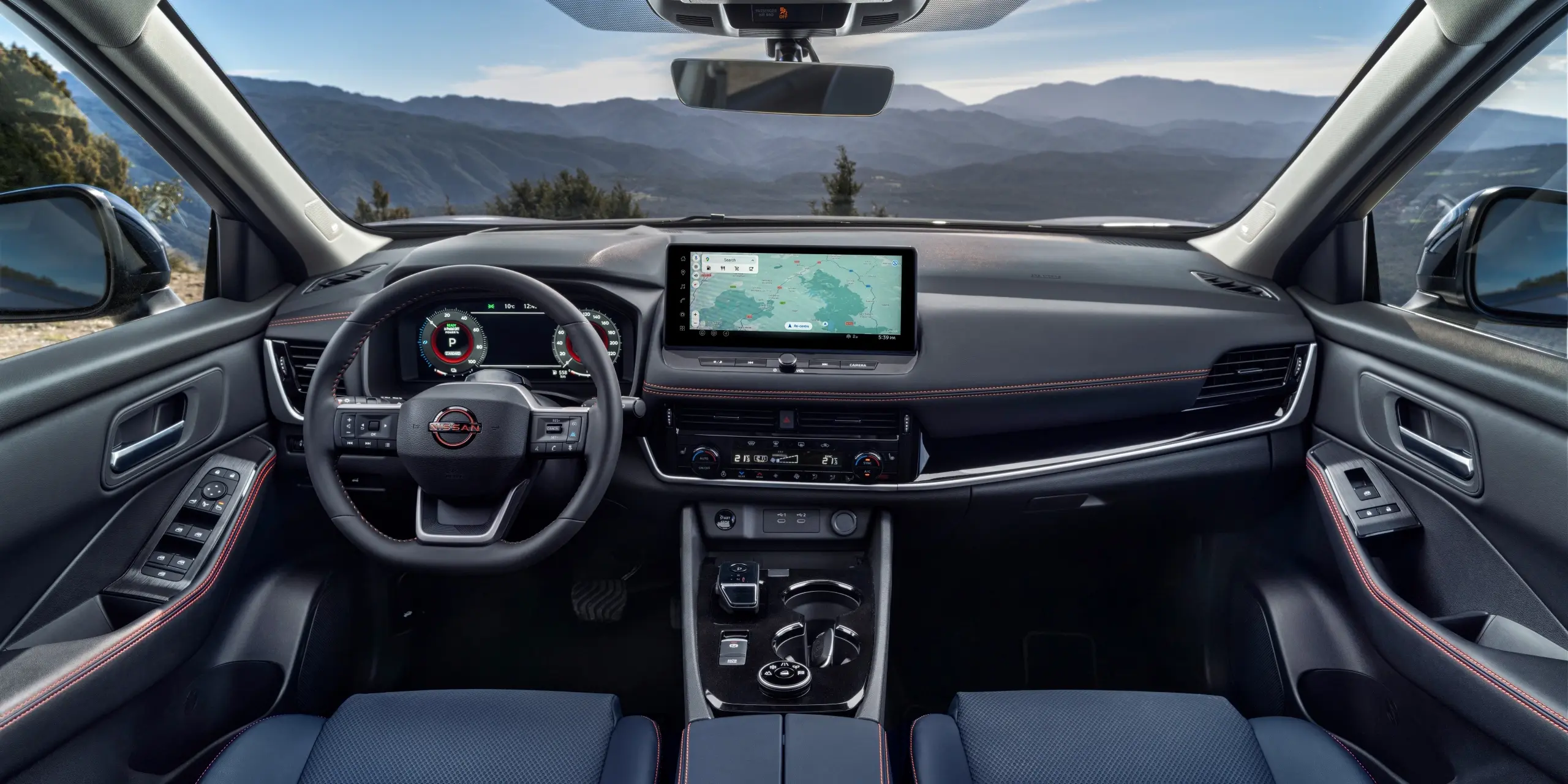 Car interior featuring a modern dashboard with a touchscreen navigation system, steering wheel, and scenic mountain view through the windshield.