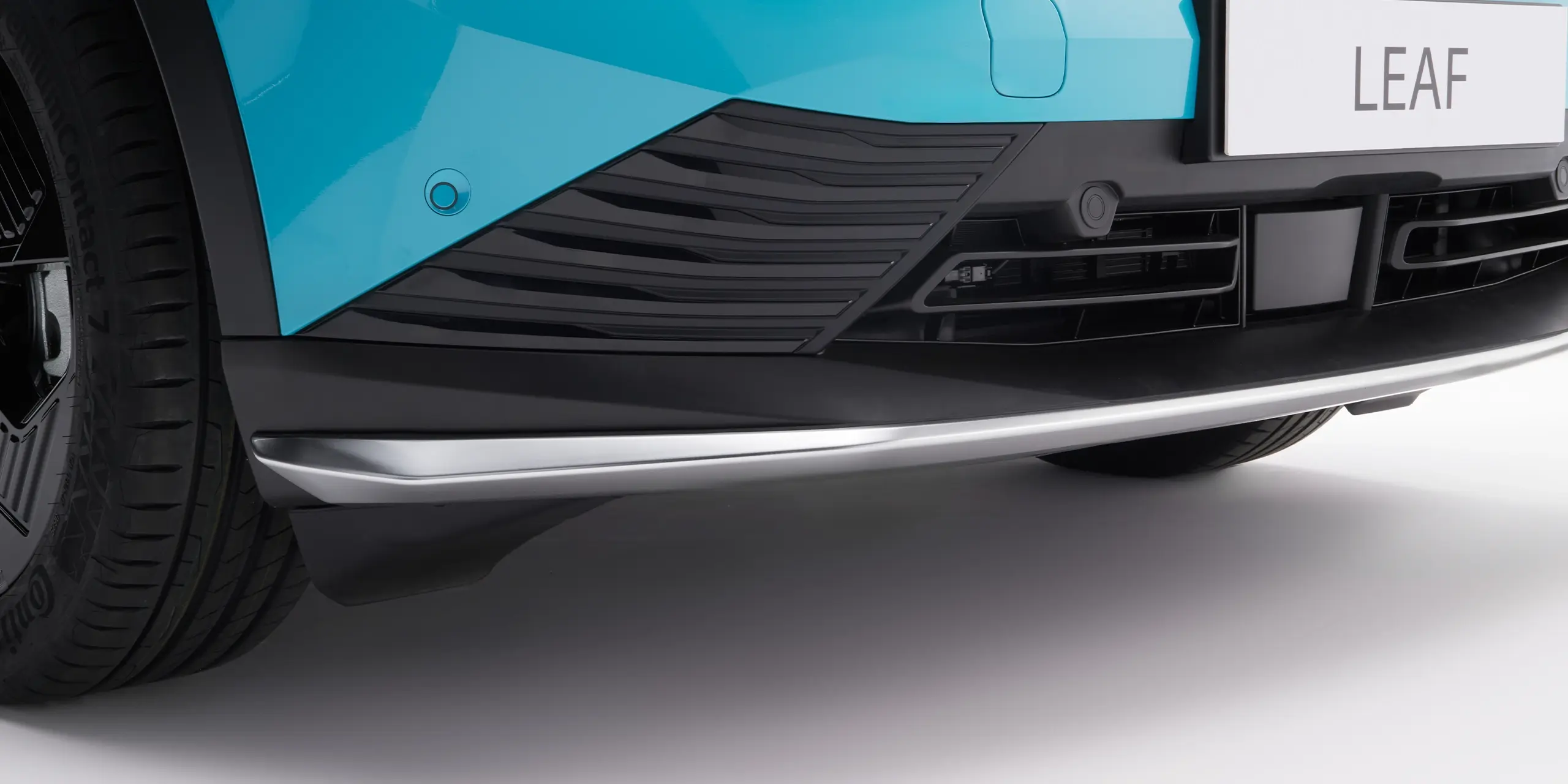 Close-up of a blue and black vehicle front bumper with a visible tire and license plate reading "LEAF."