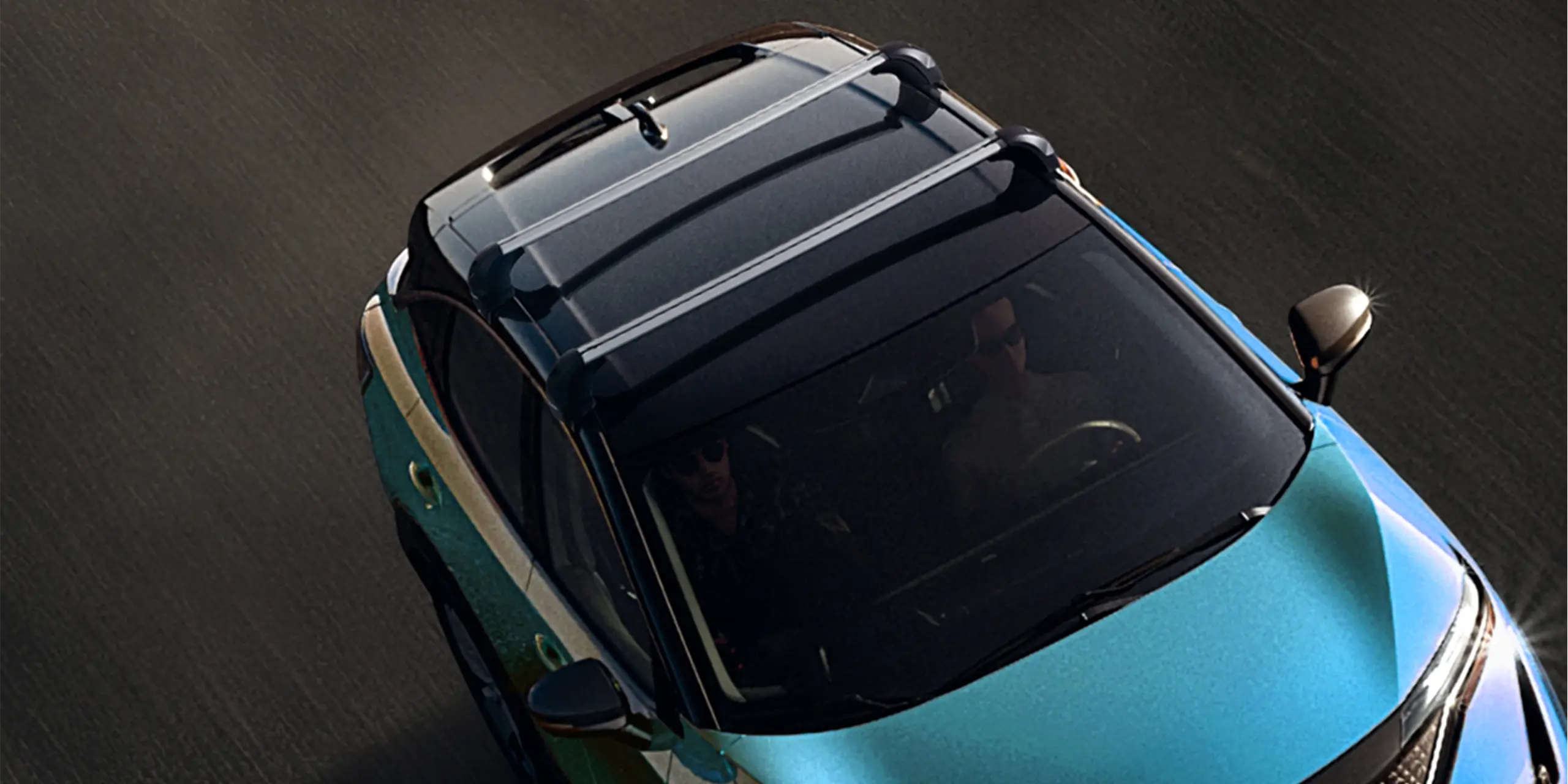 Top view of a car driving on a road, highlighting its roof and two individuals inside.