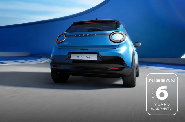Blue Nissan MICRA driving on a curved road with blue walls, showcasing its design. "Up to 6 years warranty" badge displayed.